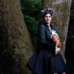 Tier Fotoshootings mit einer Frau die ein Huhn am Arm hält an einem Baum gelehnt mit einem Kranz von misslillyshats