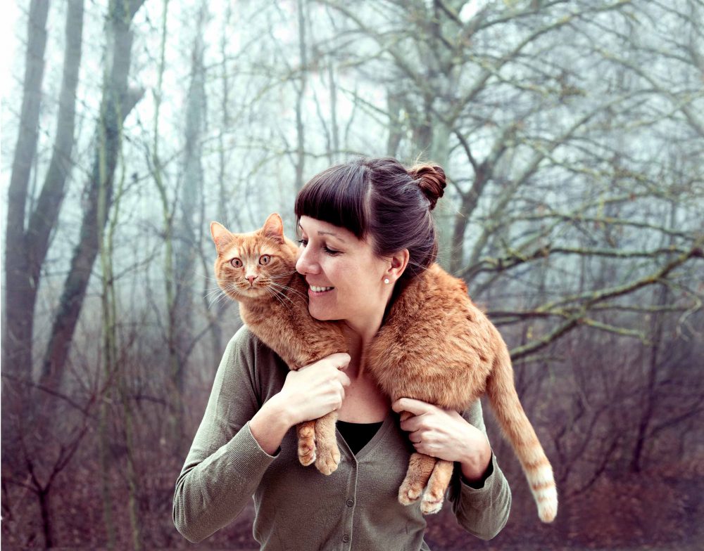 Frau mit roter Katze auf den Schultern im Hintergrund Bäume