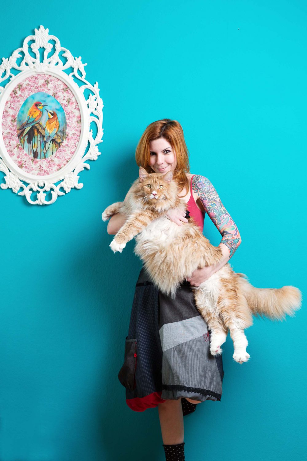 Katzenfotografie einer Frau mit grosser roter Katze im Arm vor türkisem Hintergrund